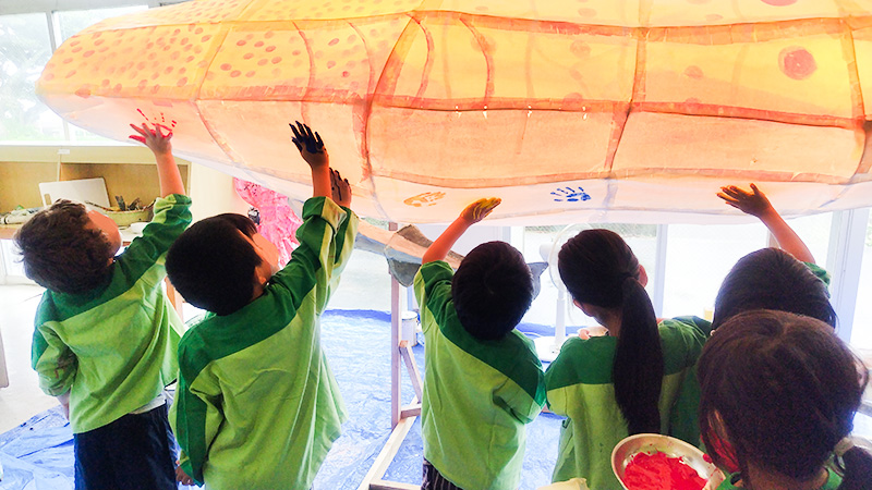 黄色いパラバルーンを空に向かって持ち上げるあゆみの森こども園の子どもたち