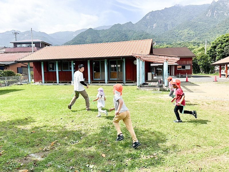 屋久島の山々を背景にした園庭で遊ぶあゆみの森こども園の子どもたち