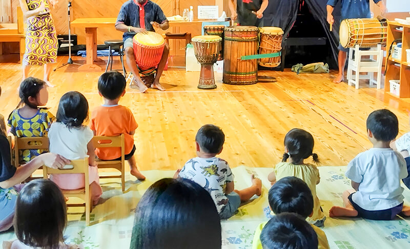 オレンジ色の服の子どもたちがジェンベで合奏するこども園の音楽活動