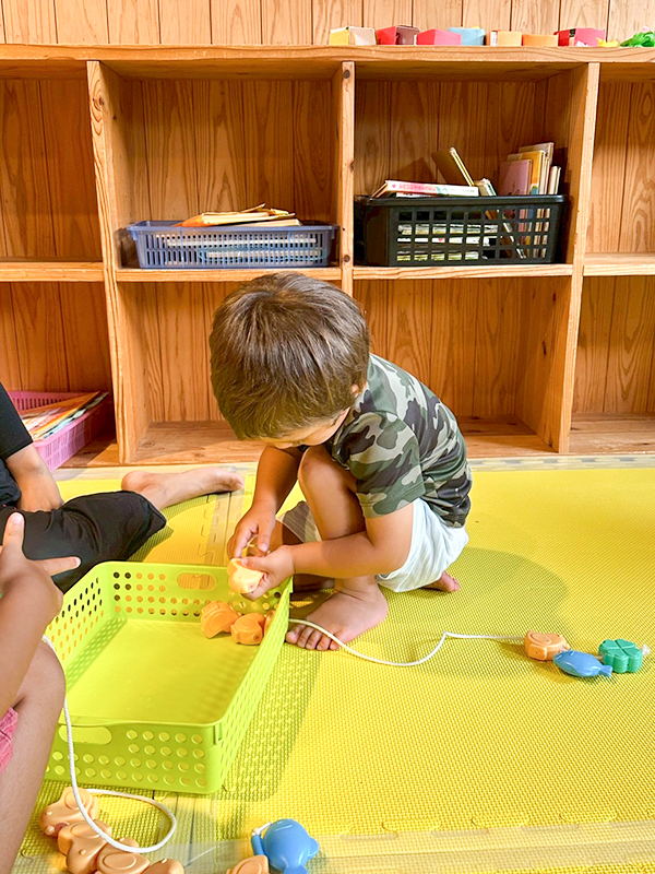 木製の棚からおもちゃを選んで遊ぶこども園の園児