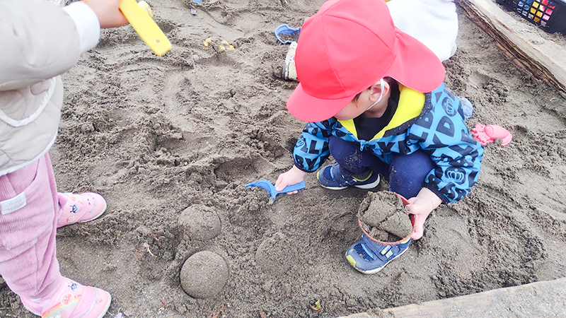 カラフルな帽子をかぶって地面で自然遊びをする園児たち