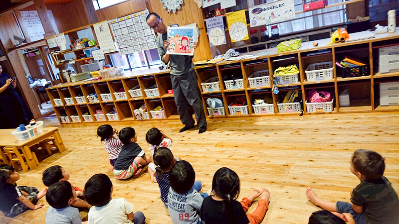 絵本棚の前で熱田園長の話を聞くあゆみの森こども園の子どもたち