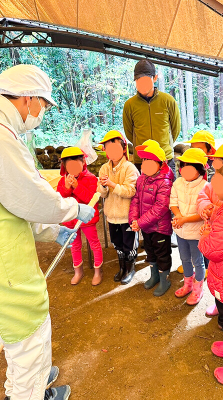 屋外で開催される熱田園長の音楽ワークショップに参加する子どもと保護者