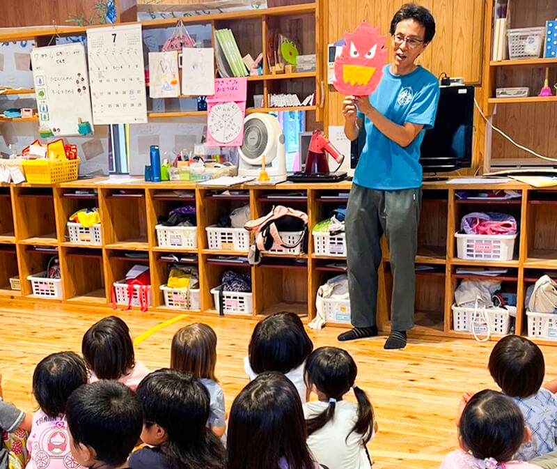 絵本棚の前で熱田園長のお話を聞くあゆみの森こども園の特別授業