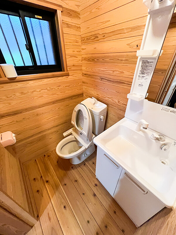 木の床が温かみを感じさせる職員寮101号室のトイレと洗面台